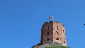 Gedimino pilies bokštas su Lietuvos vėliava žaliame kalne ryškiai mėlyname danguje